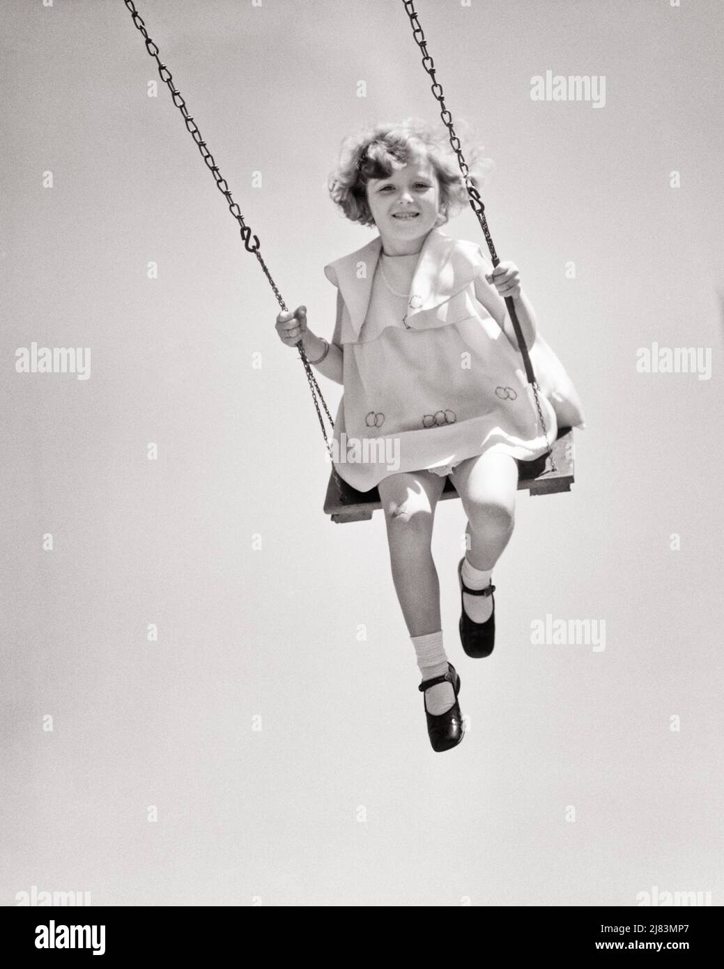 1920s 1930s SMILING LITTLE GIRL LOOKING AT CAMERA WEARING DRESS AND MARY JANE SHOES SWINGING HIGH ON PARK PLAYGROUND SWING - j3585 HAR001 HARS COMPETITION PLEASED JOY LIFESTYLE SPEED FEMALES HEALTHINESS COPY SPACE FULL-LENGTH RISK CONFIDENCE B&W EYE CONTACT SUCCESS ACTIVITY HAPPINESS PHYSICAL WELLNESS CHEERFUL STRENGTH COURAGE AND CHOICE EXCITEMENT LOW ANGLE RECREATION MARY JANE ON SMILES SWINGING GRAVITY CONCEPTUAL FLEXIBILITY JOYFUL MUSCLES STYLISH GROWTH JUVENILES BLACK AND WHITE CAUCASIAN ETHNICITY HAR001 OLD FASHIONED Stock Photo