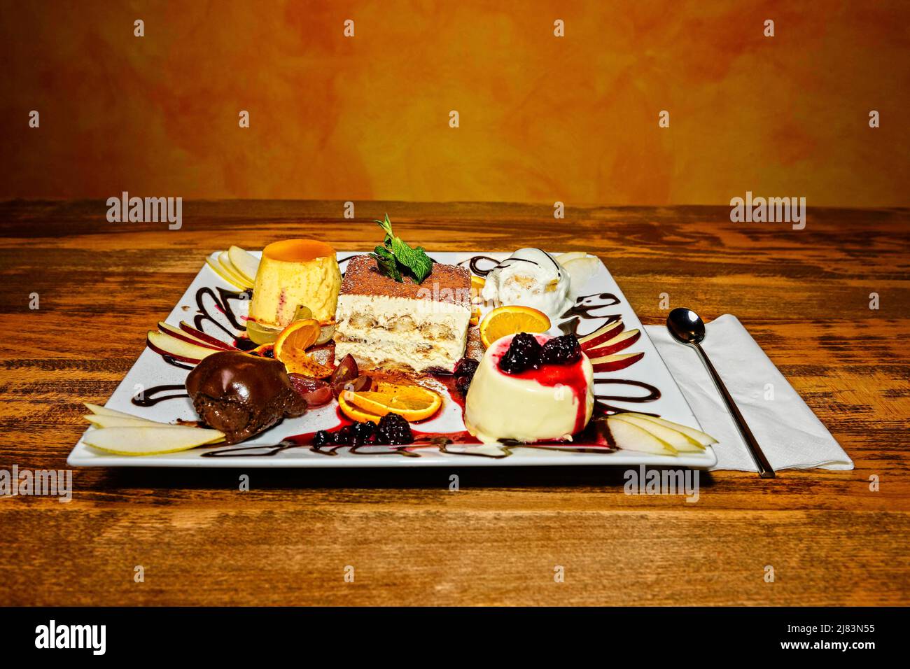 Foodfotografie, Teller mit Auswahl an italienischen Suessspeisen wie Tiramisu, Profiteroles und Panna Cotta auf hoelzernem Tisch Stock Photo