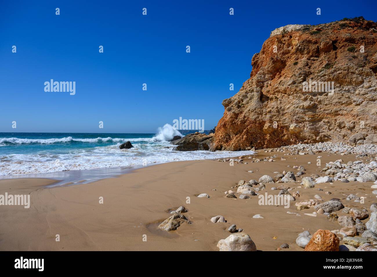 Portugal hat an der Algarve viele Steilkuesten mit feinem Sandstrand und hohen Wellen des Atlantik. Der blaue Himmel mit der weissen Gischt ist ein Stock Photo