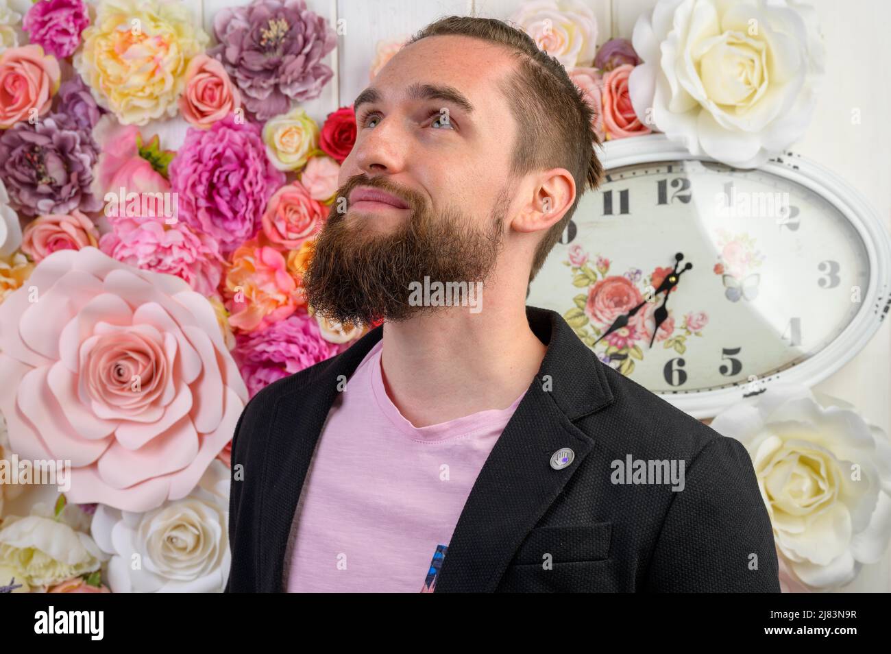 Portrait eines jungen Mannes mit langem Vollbart und kurzen Haaren bekleidet mit einem schwarzen Sakko und einem rosa Shirt. Sein Blick richtet sich Stock Photo