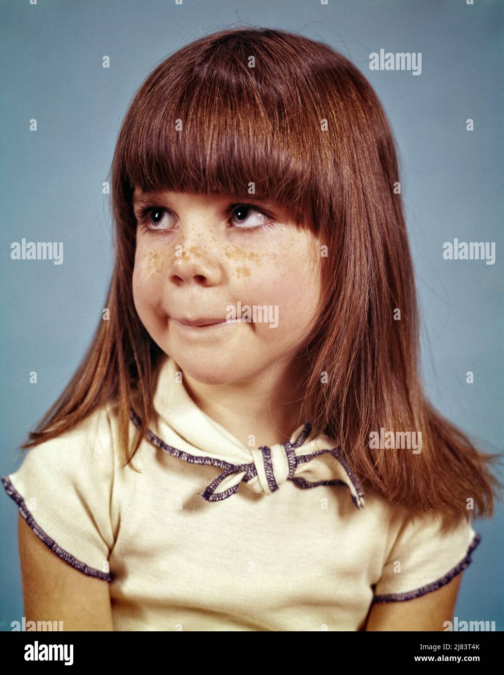 1970s BRUNETTE LITTLE GIRL FRECKLES ON NOSE LONG HAIR BANGS WITH GOOFY FACIAL EXPRESSION LOOKING UP AND TO THE SIDE SILLY GRIN - kj7426 HAR001 HARS EXPRESSIONS BRUNETTE HUMOROUS HEAD AND SHOULDERS AND COMICAL UP COMEDY GOOFY PLEASANT AGREEABLE CHARMING GRIN JUVENILES LOOKING UP LOVABLE PLEASING ADORABLE APPEALING BANGS CAUCASIAN ETHNICITY HAR001 INNOCENCE OLD FASHIONED Stock Photo