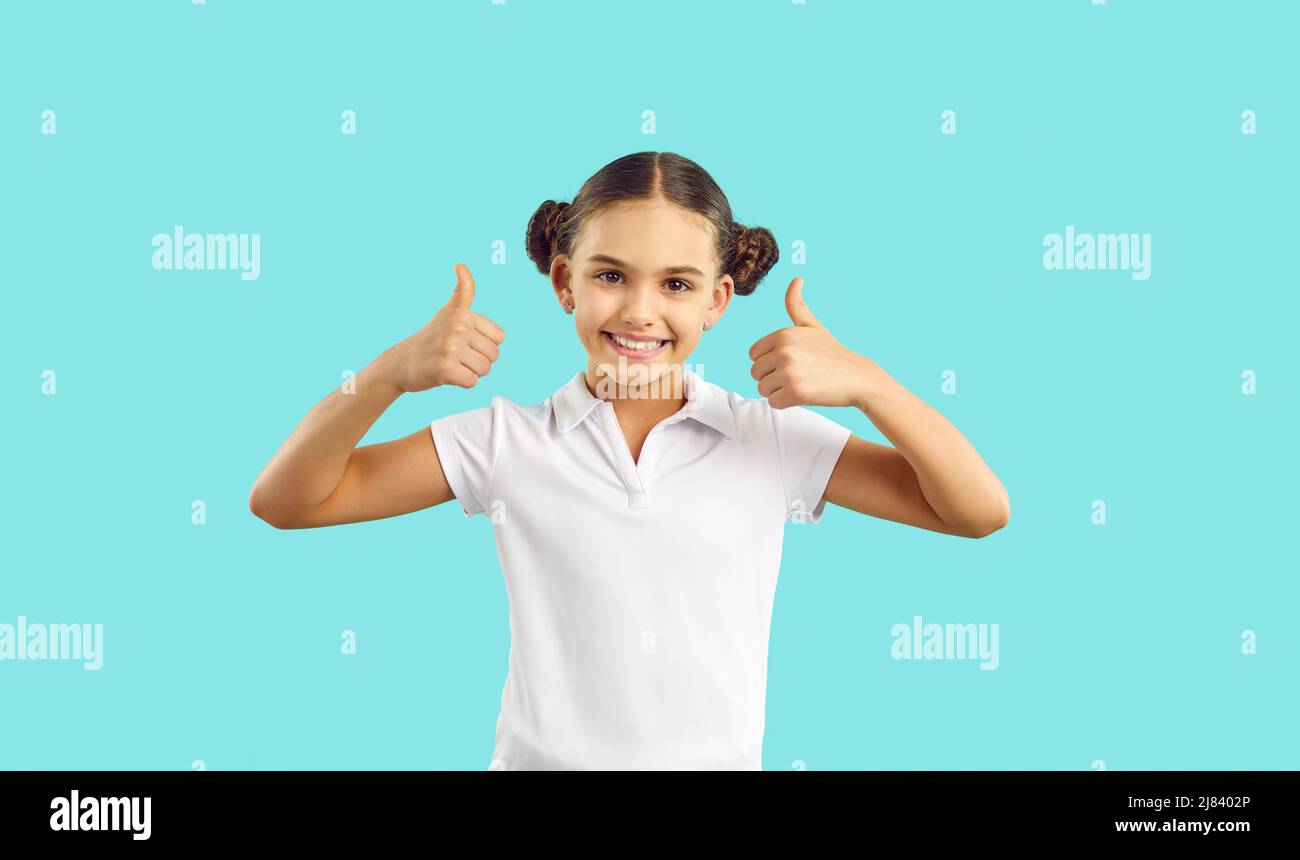 Happy pretty girl in T shirt standing isolated on blue, smiling and giving thumbs up Stock Photo