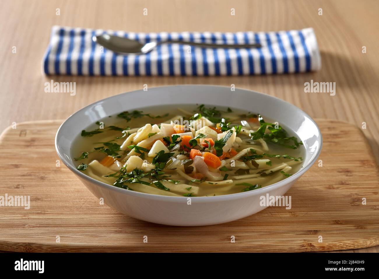 Warm vegetable soup with noodles and fresh chopped herbs on wood Stock Photo