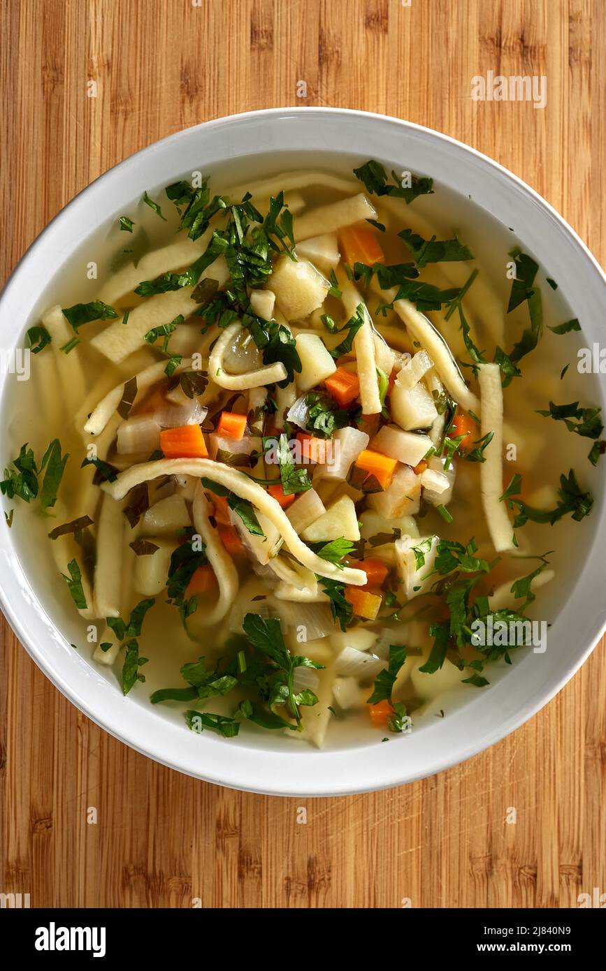 Warm vegetable soup with noodles and fresh chopped parsley on wood - top view Stock Photo