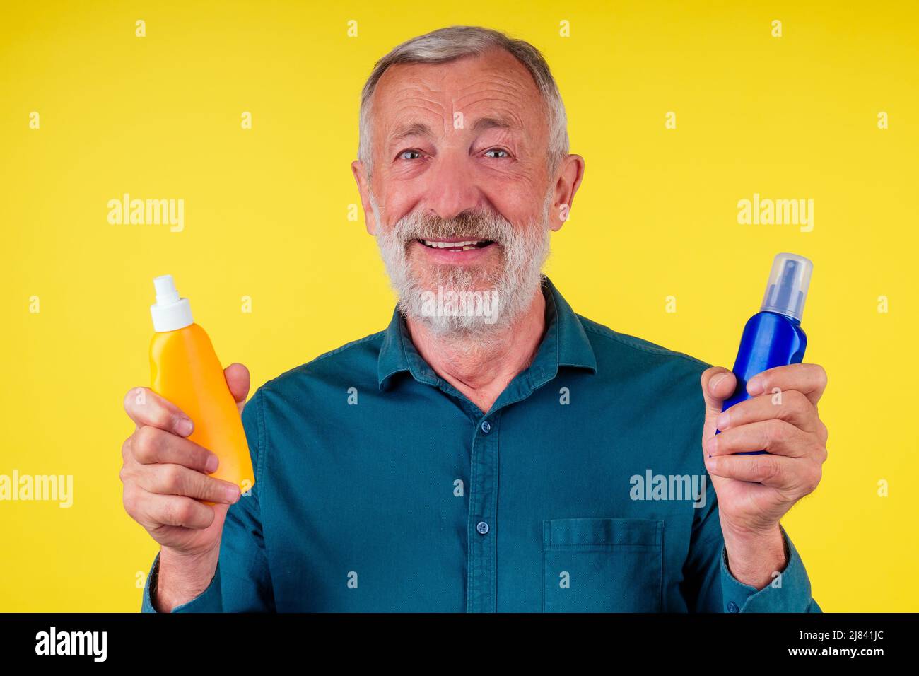 Senior man choosing sun protection cream between two spray bottle in studio yellow background Stock Photo