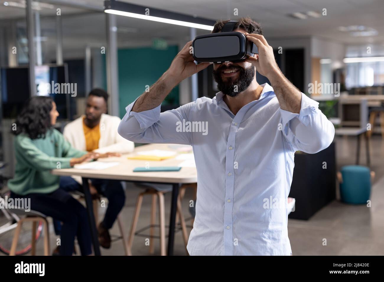Smiling caucasian businessman wearing virtual reality simulator at modern workplace Stock Photo
