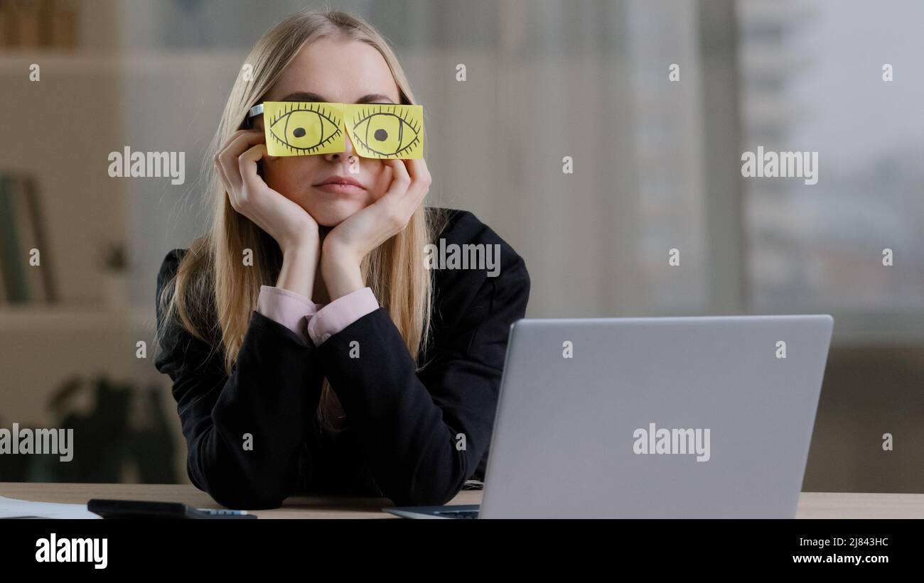 Tired sleepy funny lazy caucasian business woman with sticky notes on eyes glasses with stickers. Fatigued female worker napping at workplace sit at Stock Photo