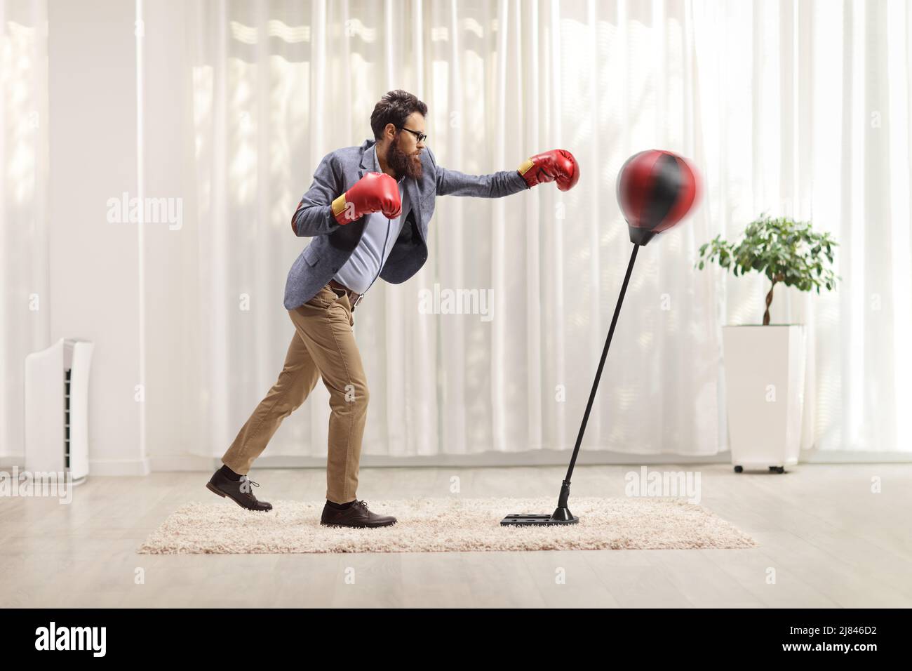 Man in formal clothes boxing with gloves into a punch bag inside a room