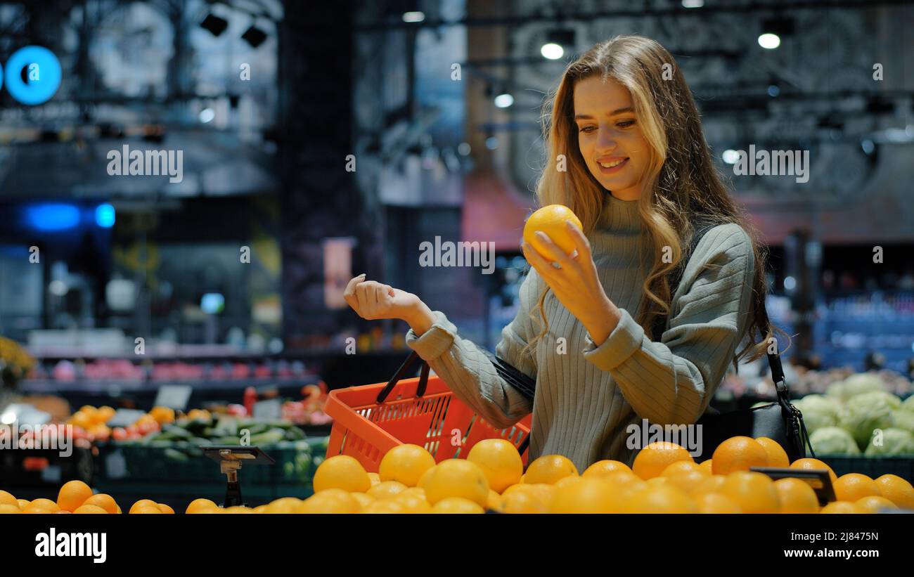 Caucasian woman consumer female shopper girl buyer with shopping basket at grocery store in supermarket choosing orange juicy citrus delicious fruit Stock Photo