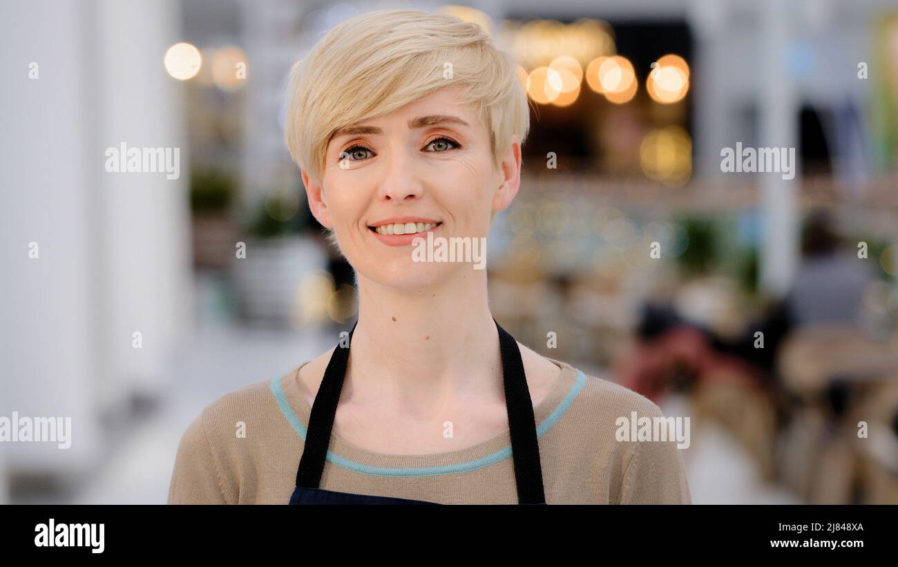 Mature adult middle aged 40s woman lady restaurant cafe worker owner looking at camera smiling toothy friendly smile happy female waitress saleswoman Stock Photo