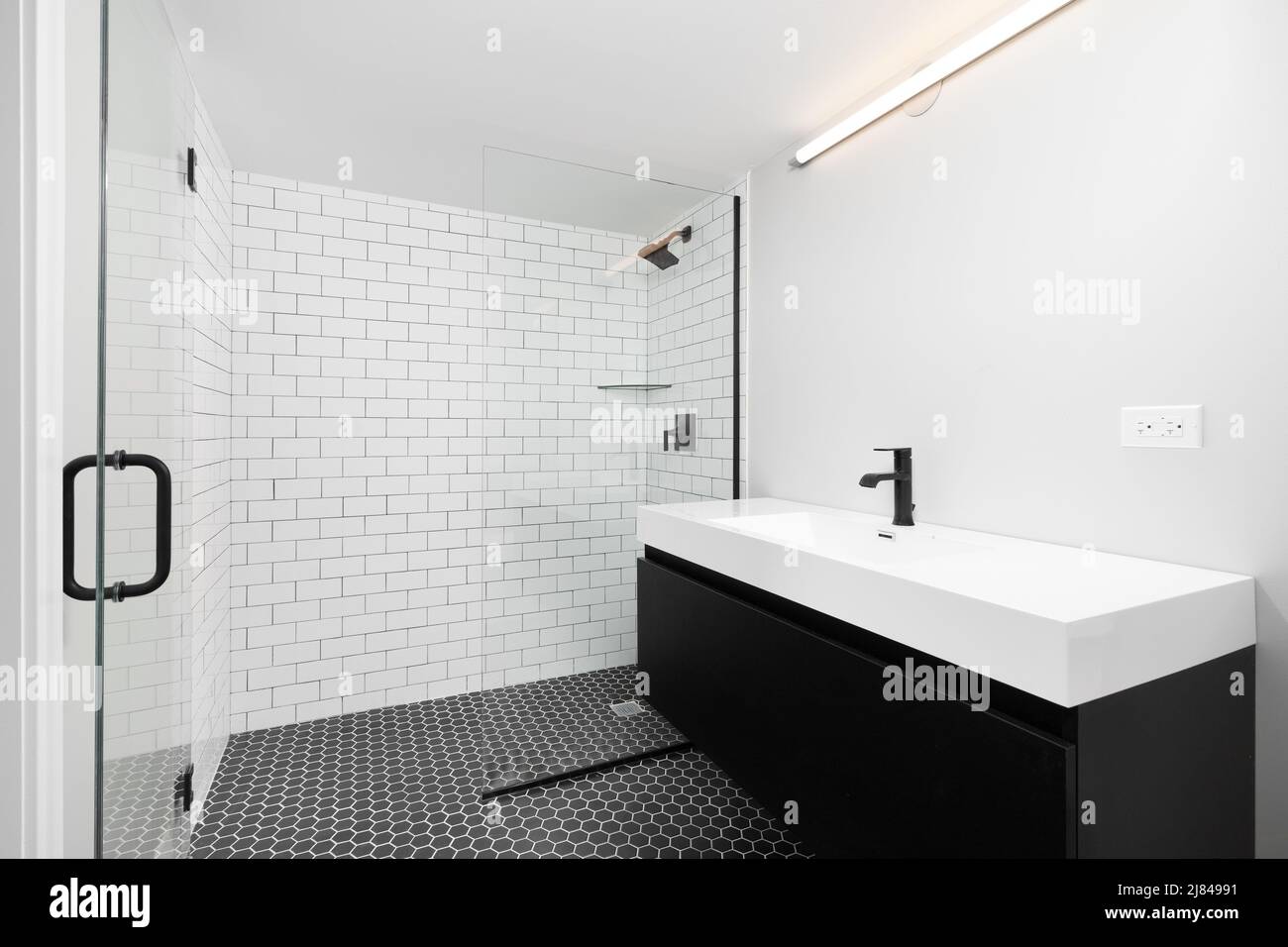 A renovated bathroom with a black vanity cabinet, white vessel sink and  black faucet, black hexagon tile flooring, and a white subway tile shower  Stock Photo - Alamy, image size:1300x956