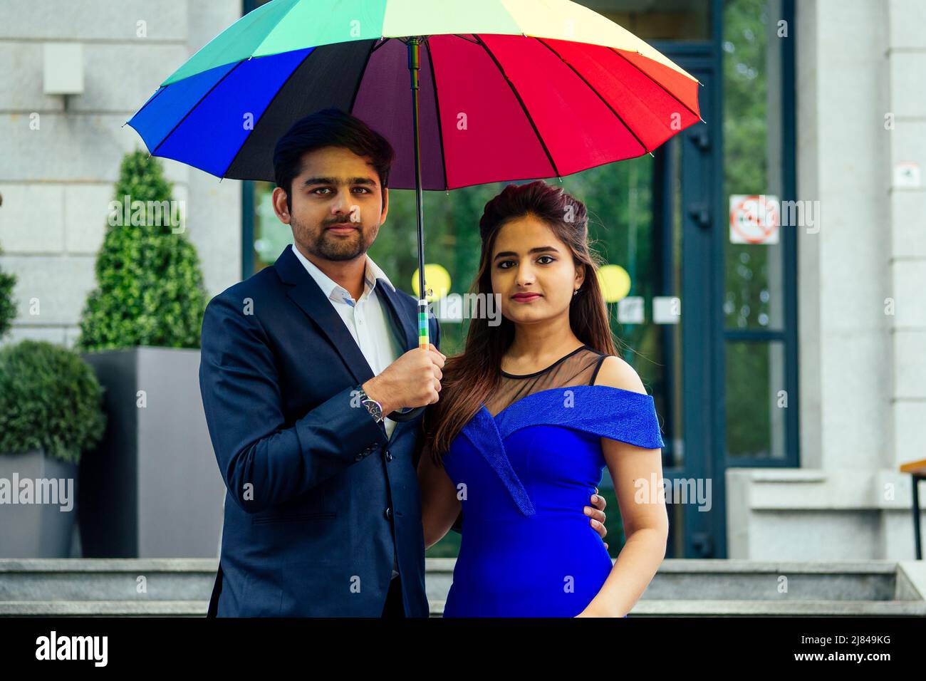 indian woman in long evening blue dress spinding romantic time together with lover handsome boyfriend under multi-colored rainbow umbrella europe Stock Photo