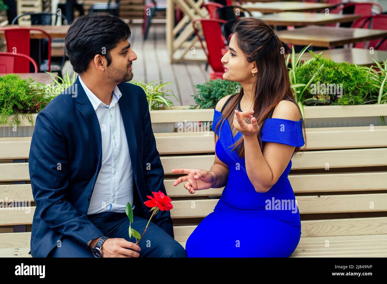 long haired brunette indian woman in blue dress with her handsome boyfriend having dating getting bored .man giving rose to his girlfriend bad Stock Photo