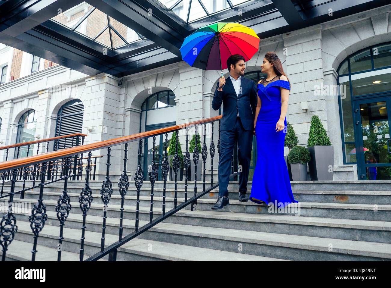 indian woman in long evening blue dress spinding romantic time together with lover handsome boyfriend under multi-colored rainbow umbrella europe Stock Photo