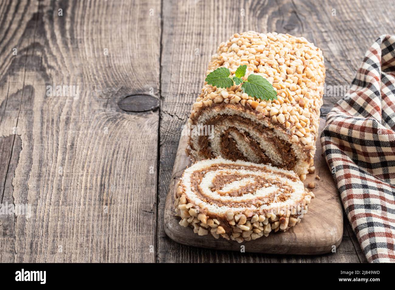 Sponge  cake roll covered with nuts on wooden table Stock Photo