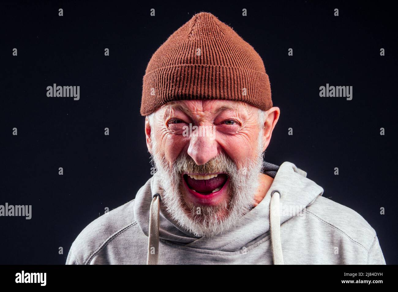portrait of sad old senior male tramp wearing warm brown hat and leaky gloves,holding metal canned bank jar for money alms in studio black background Stock Photo