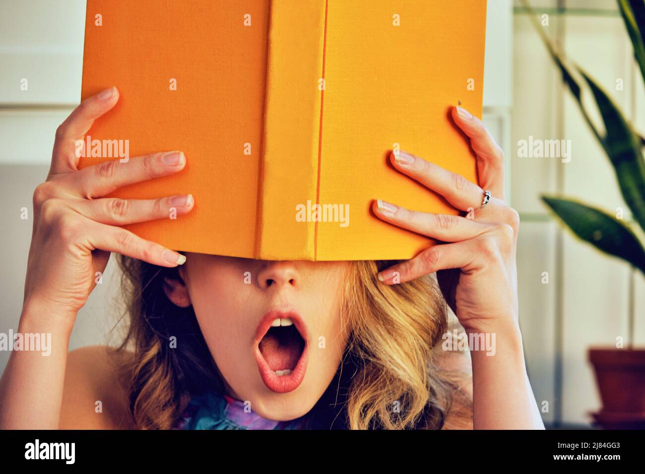 young shocked college woman with book in hands covering face library book store Stock Photo