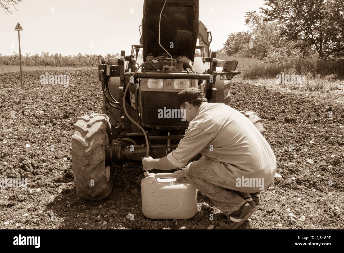 Farmer sucking diesel oil from a tractor with a rubber hose. Reference to the current expensive fuel in agriculture. Stock Photo