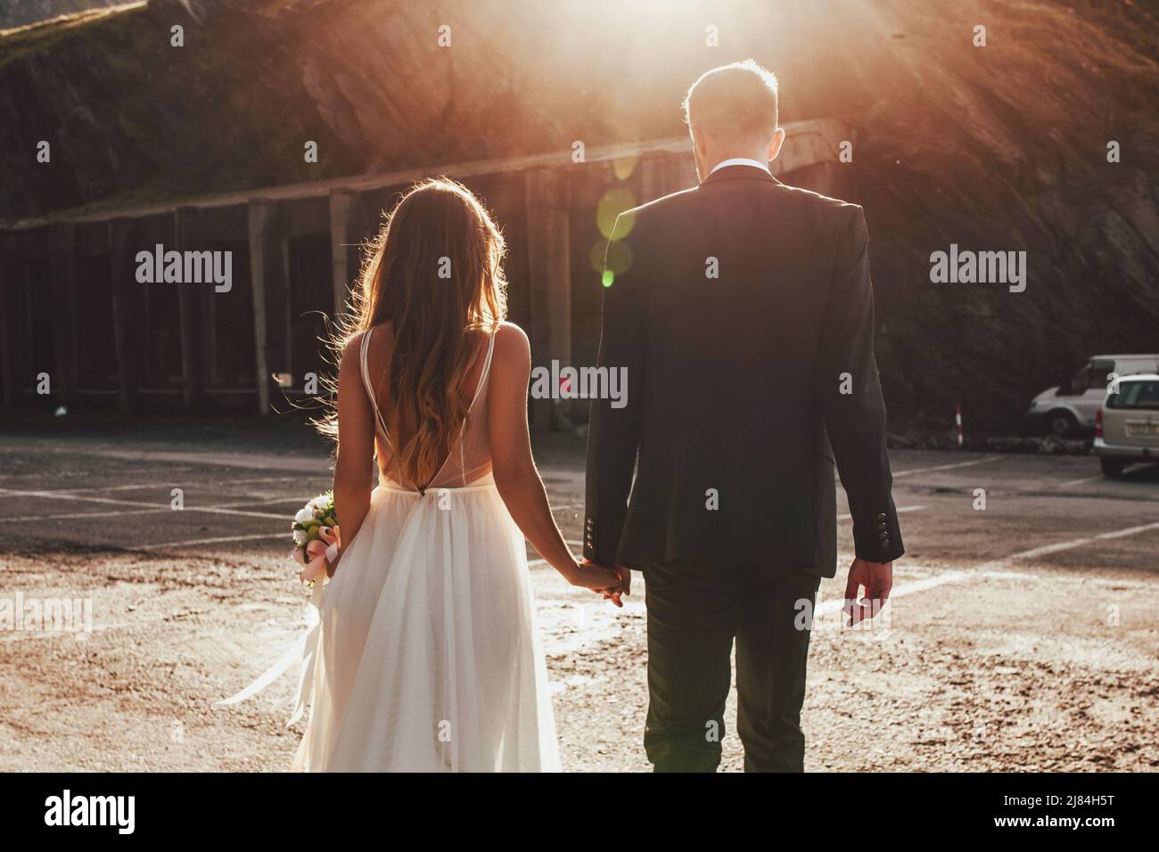Back view of bride and groom walking hand in hand along the asphalt ...