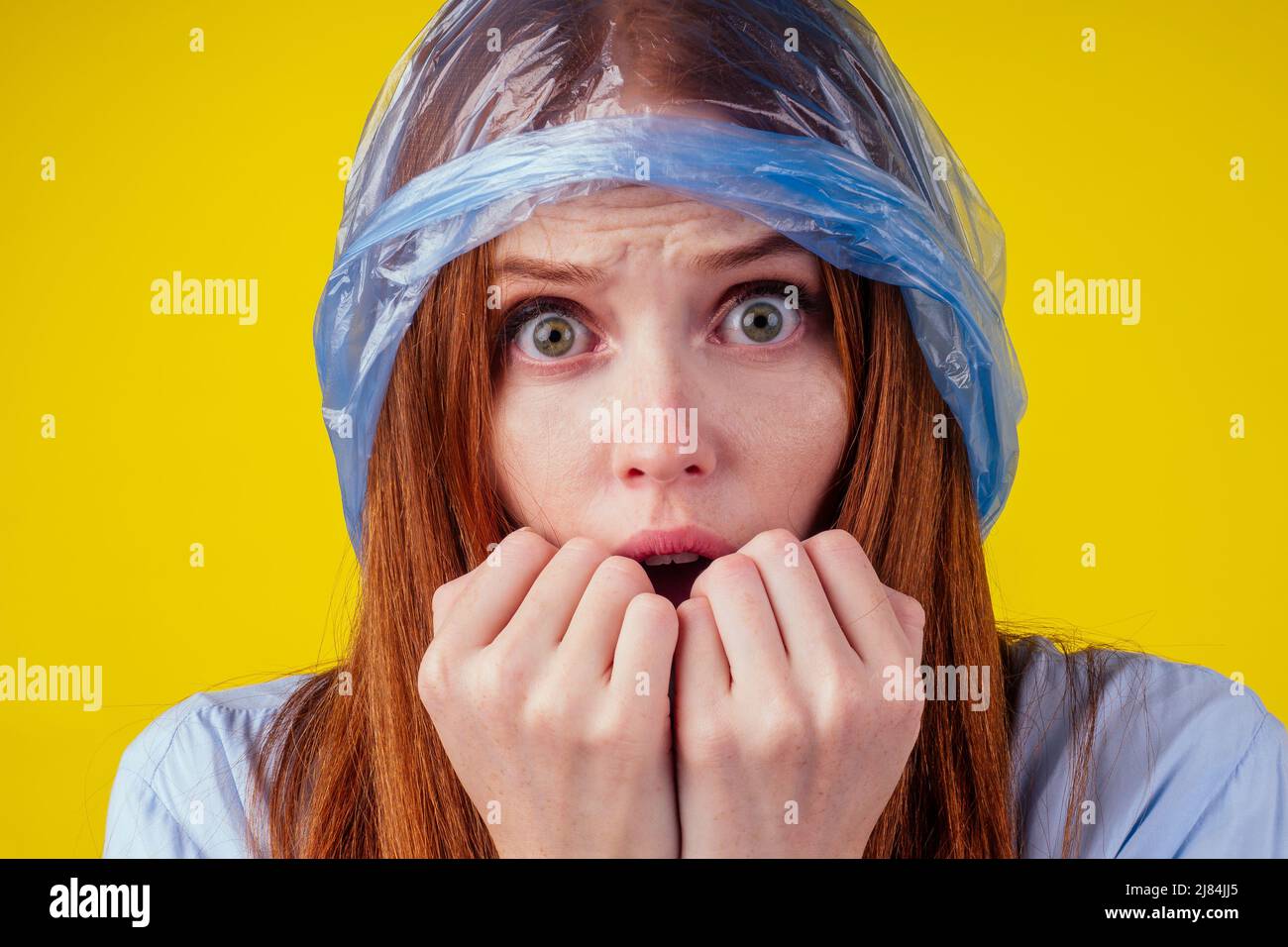 redhaired ginger european woman suffocation head in blue polyethylene package in studio yellow background. eco pollution cellophane film concept Stock Photo
