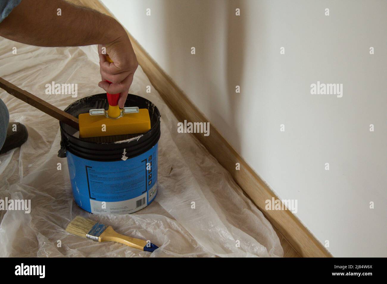Hand of a painter wetting brush in paint bucket while painting a house