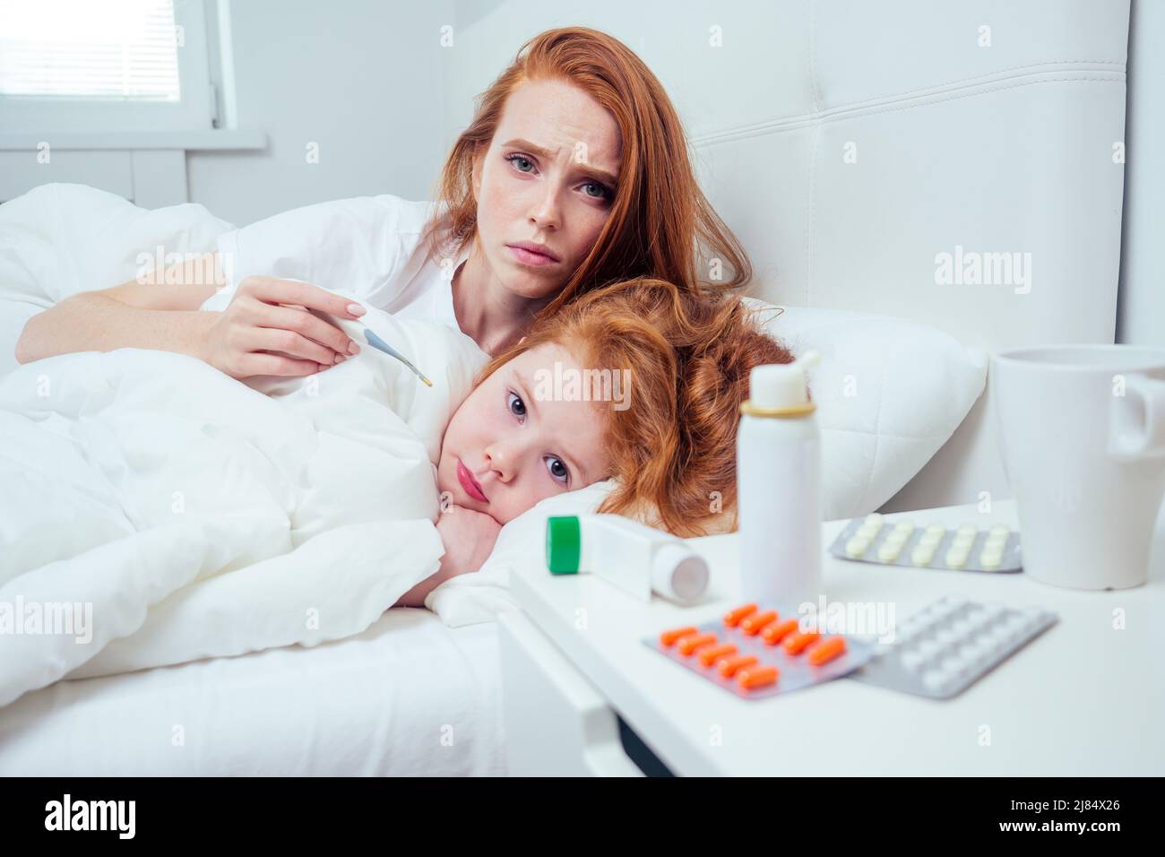 redhaired ginger woman and her ill child taking the temperature at morning Stock Photo