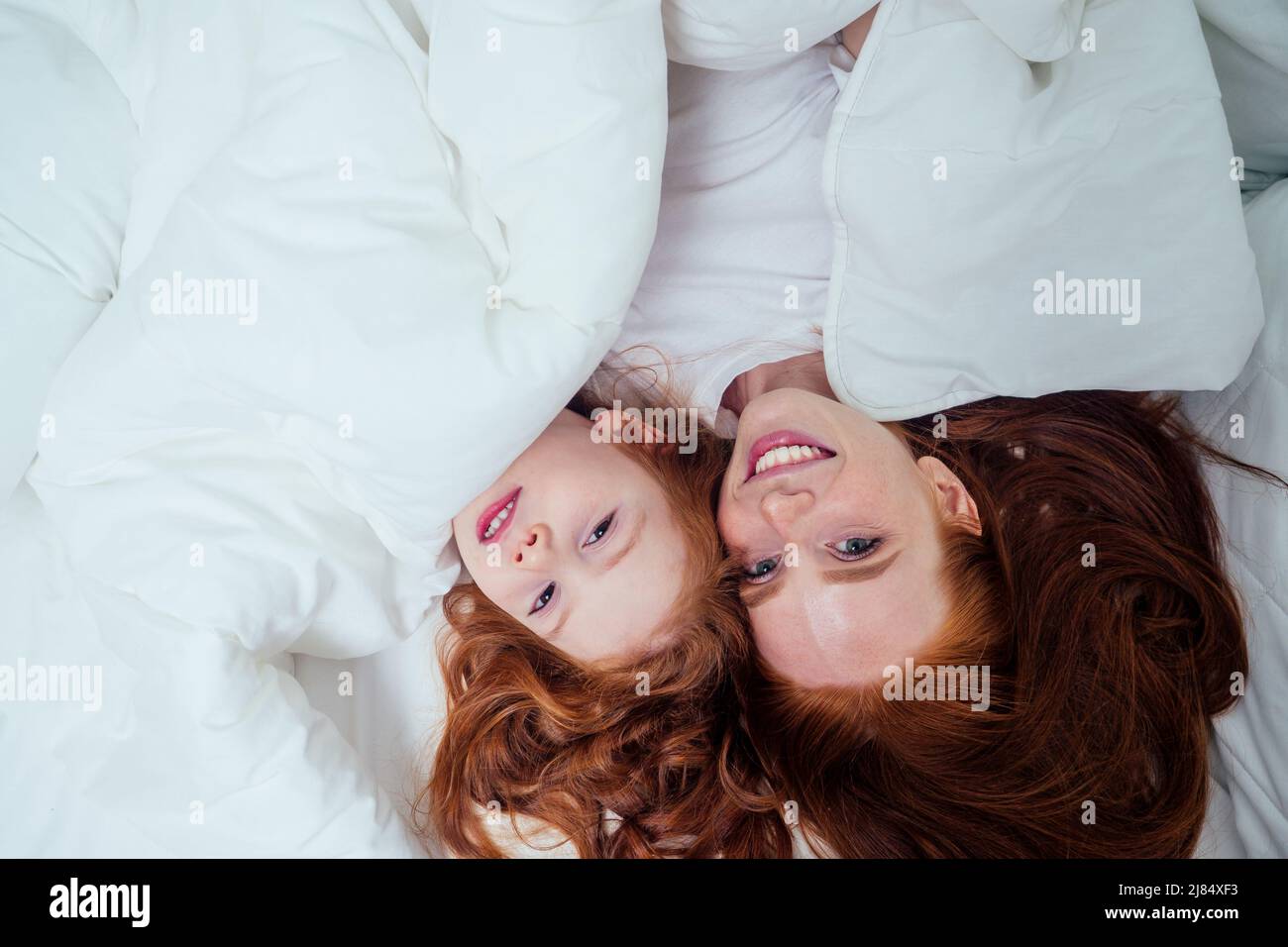 two happy redhaired ginger girls playing hide and seek under white blanket Stock Photo