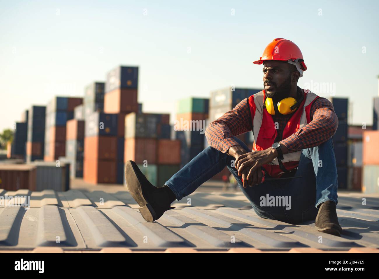 African American male technician or engineer. Sit near a container and look tired and sleepy or unemployed. Logistics industrial cargo mover concept. Stock Photo