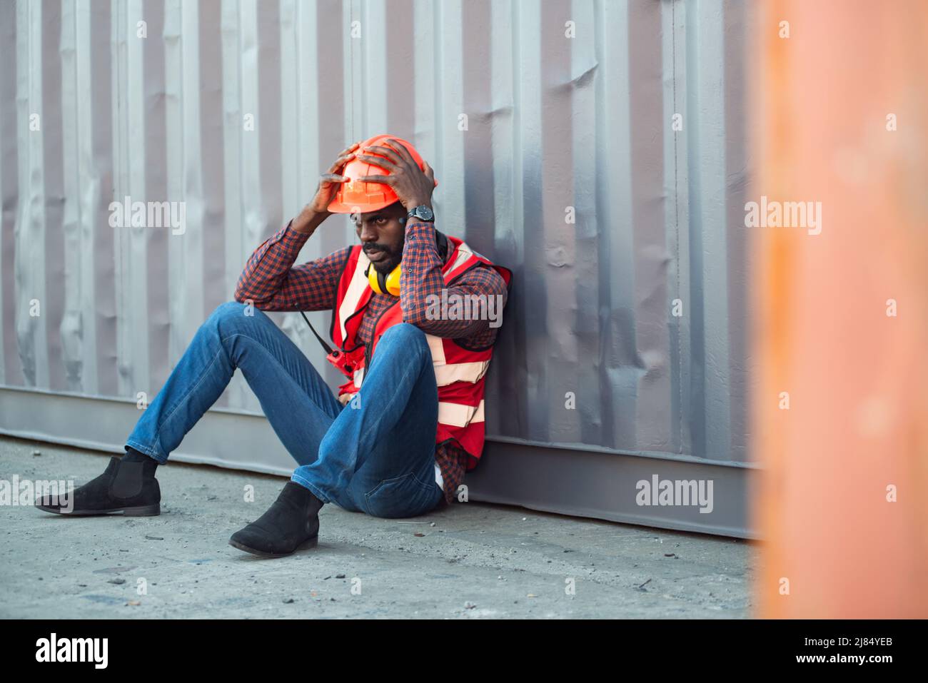 African American male technician or engineer. Sit near a container and look tired and sleepy or unemployed. Logistics industrial cargo mover concept. Stock Photo