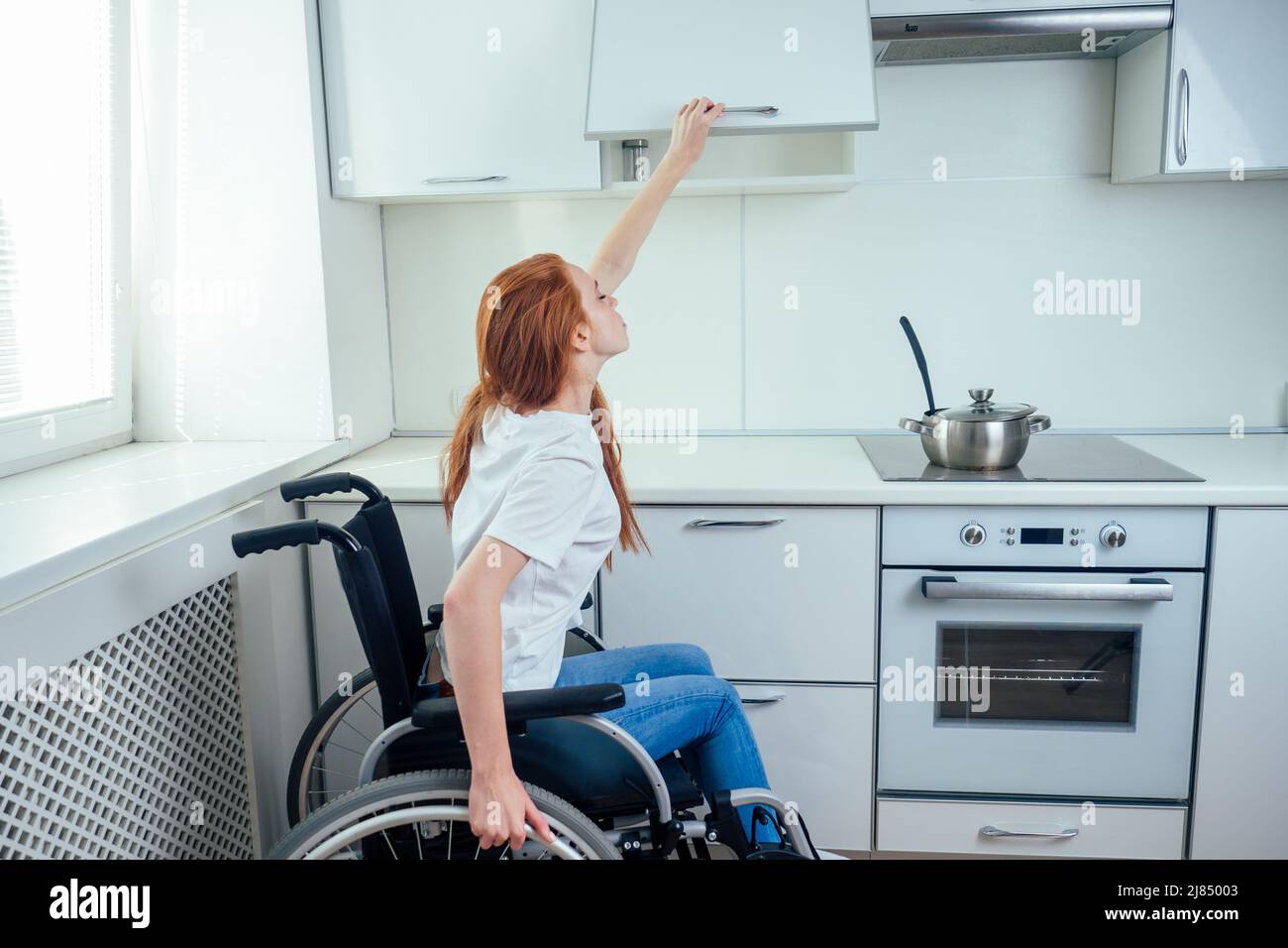 https://c8.alamy.com/comp/2J85003/disabled-redhaired-ginger-woman-in-wheelchair-preparing-meal-in-kitchentry-to-reaching-the-top-shelf-2J85003.jpg