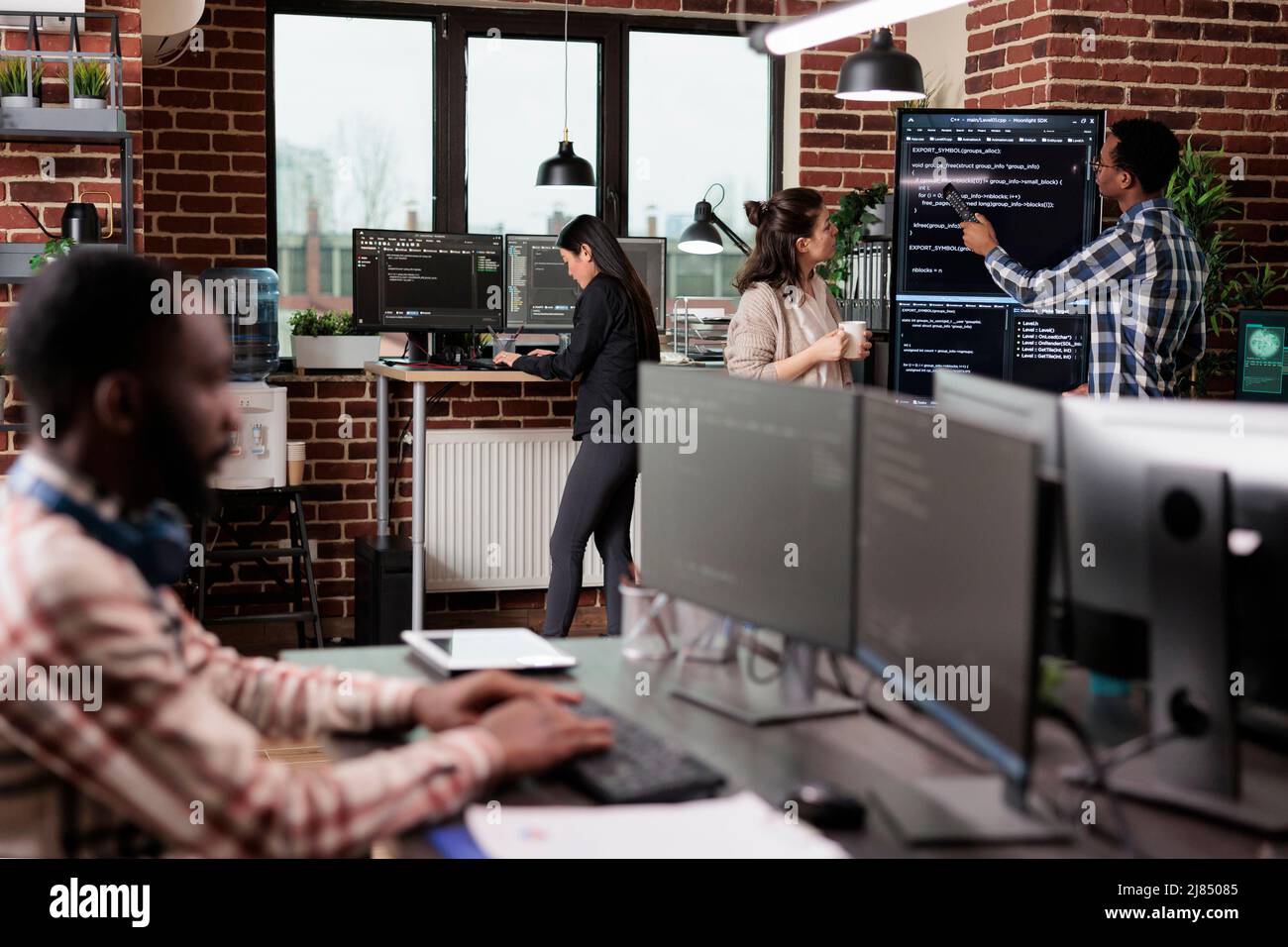Tech engineers team leader pointing out mistake in application source code. Software developers standing near vertical screen talking about interface bug and slow rate of processing data. Stock Photo