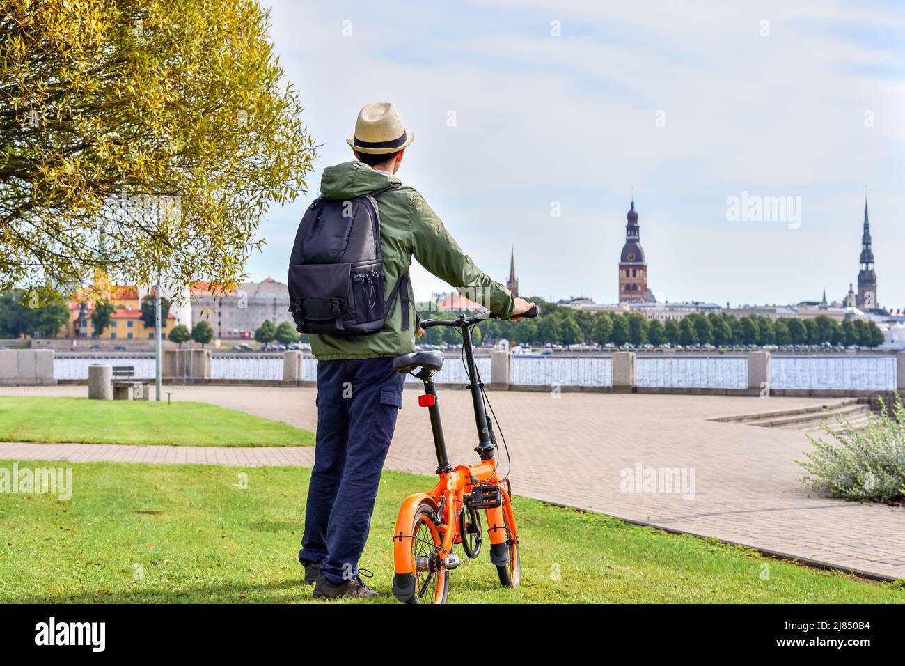 Man standing with a bicycle in a city park near the Daugava River against the backdrop of the old city of Riga, Latvia. Stock Photo