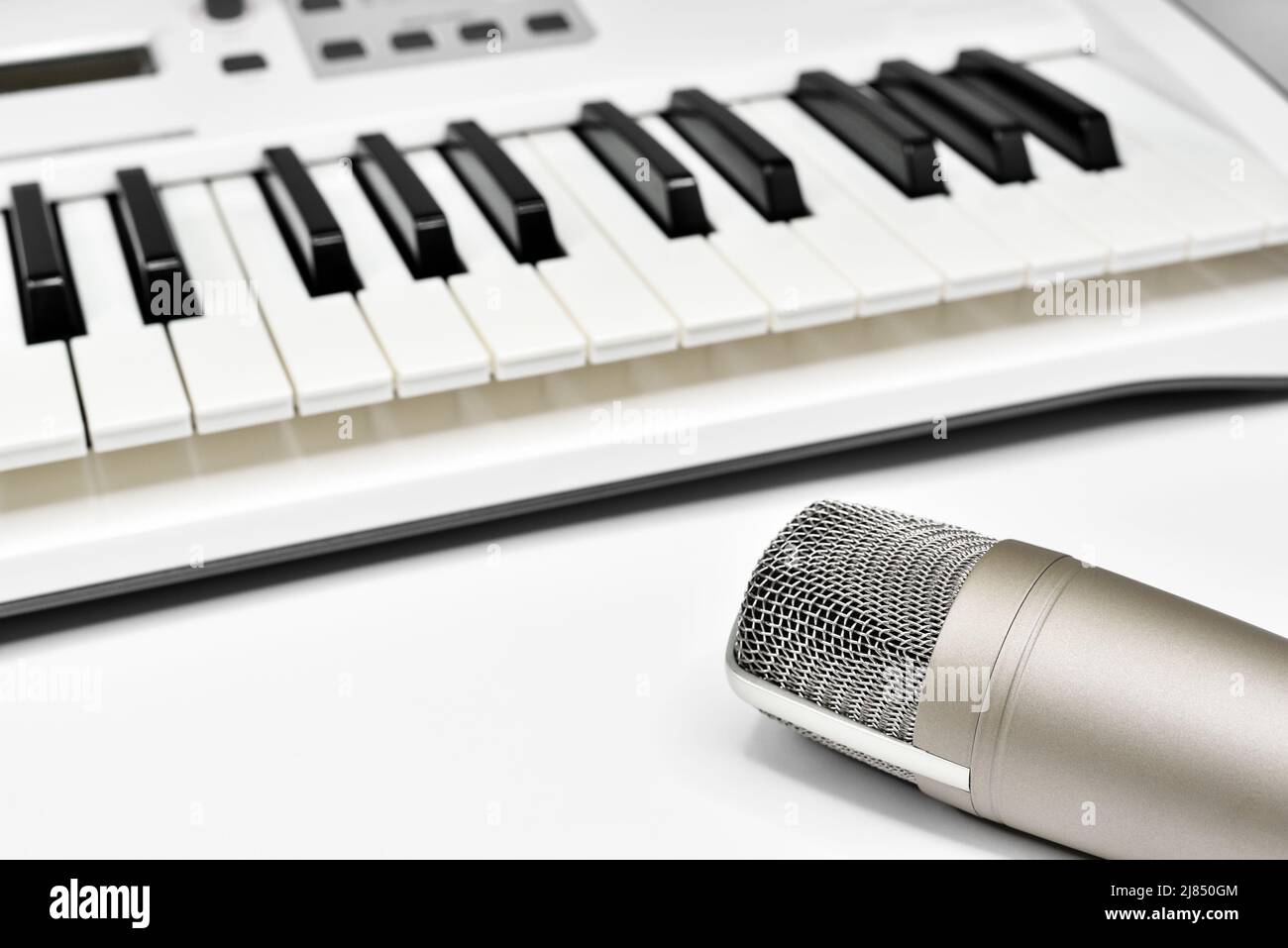 Professional studio microphone against blurred synthesizer keyboard background. Professional studio gear for voice and music recording. Stock Photo