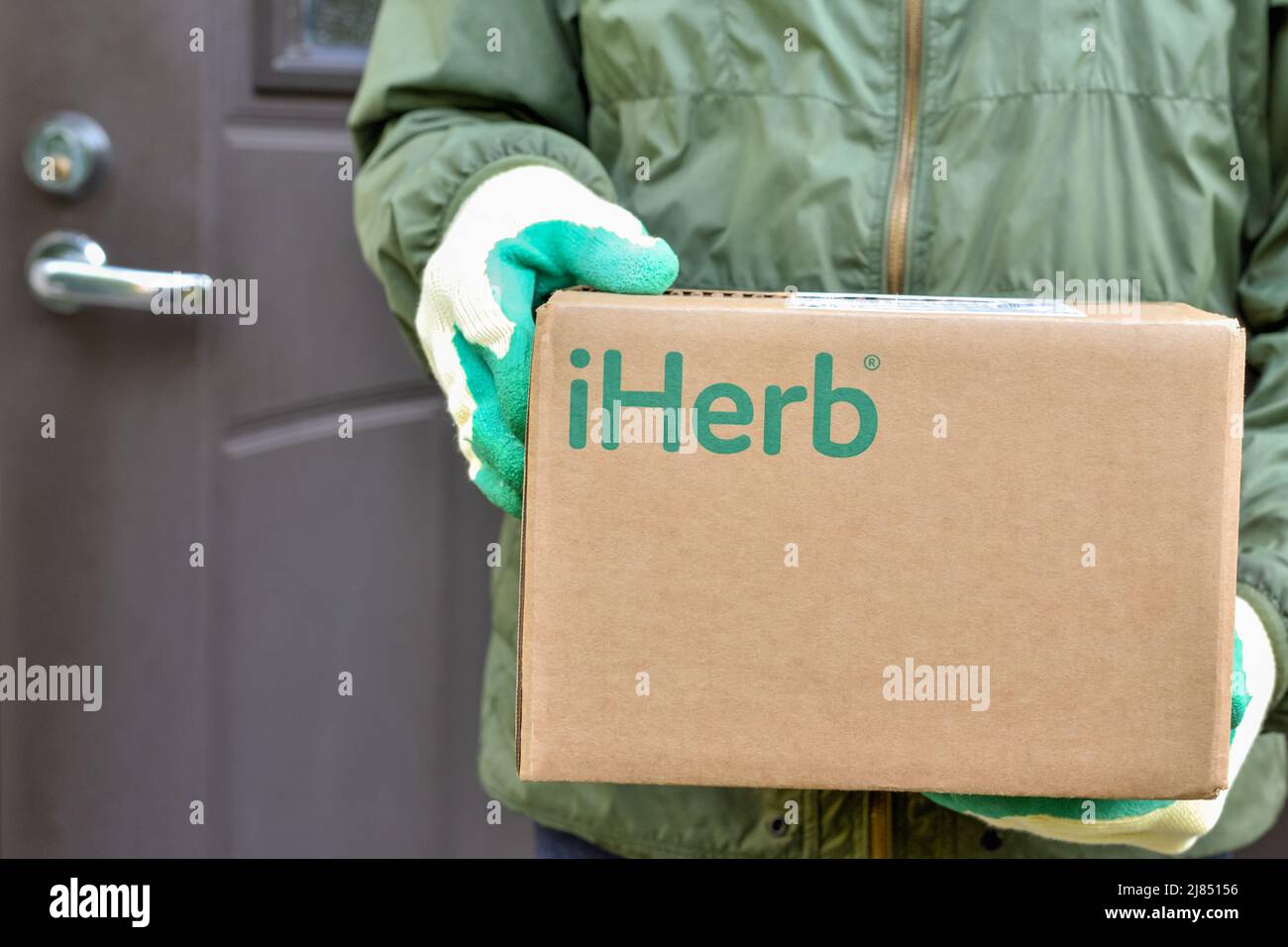 Logo iHerb on cardboard box in courier hands. iHerb is an herbal products company, provides and delivers health and wellness products Stock Photo