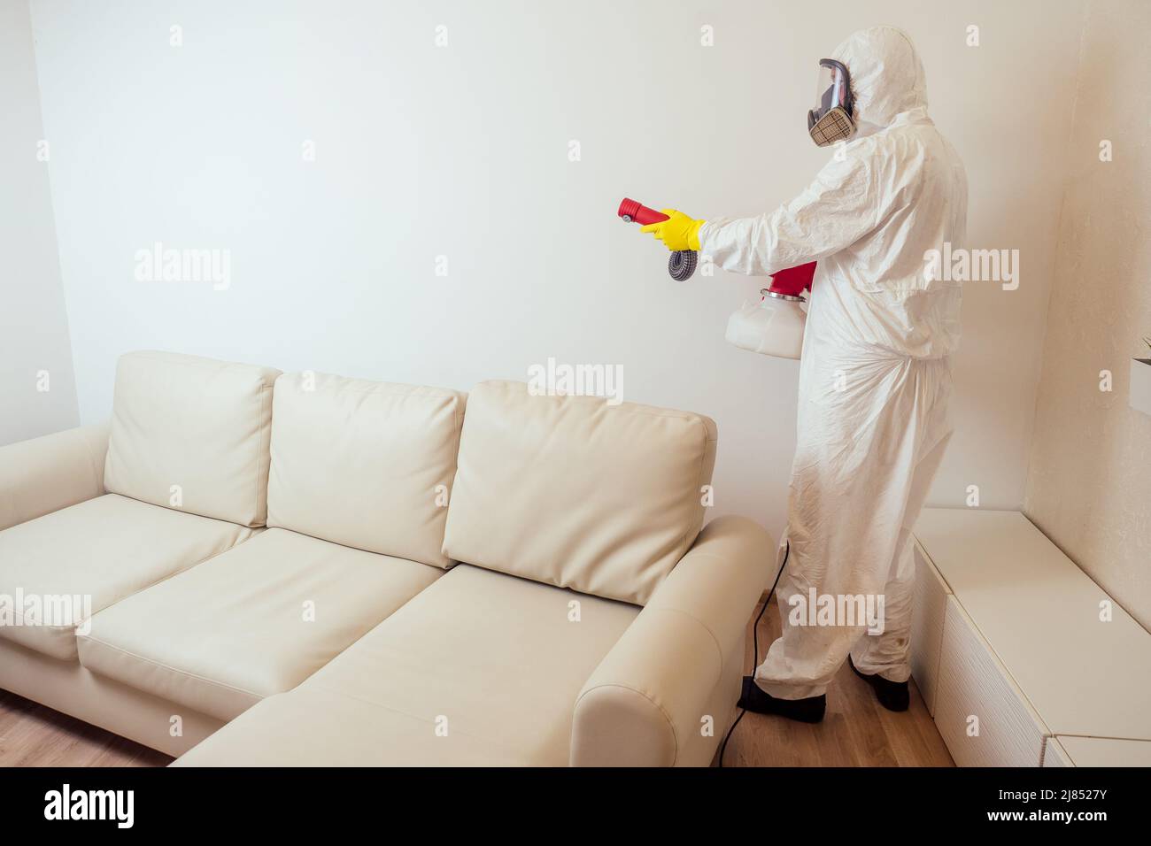 pest control worker in uniform spraying pesticides under couch in