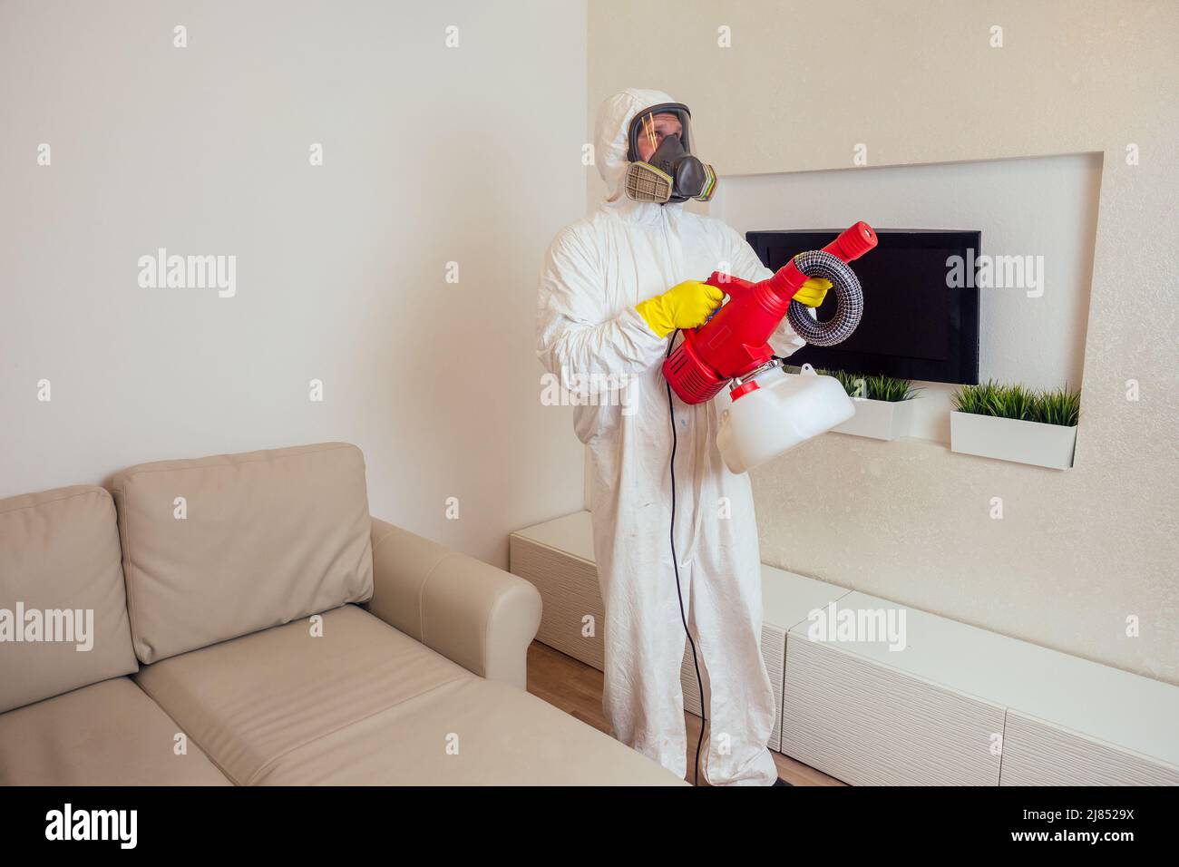 pest control worker in uniform spraying pesticides under couch in