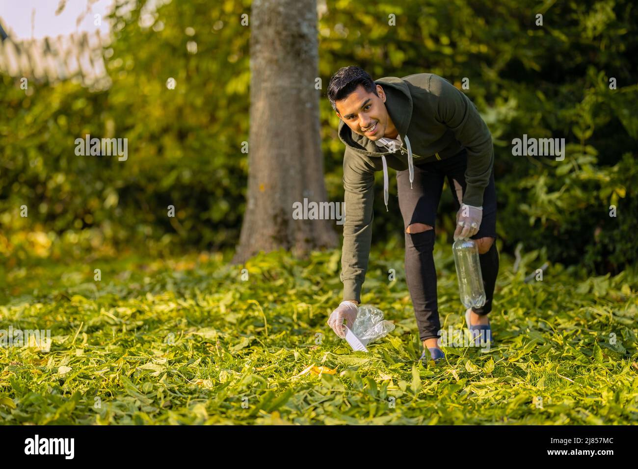 Smiling and committed volunteer cleaning garbage on grass in nature Stock Photo