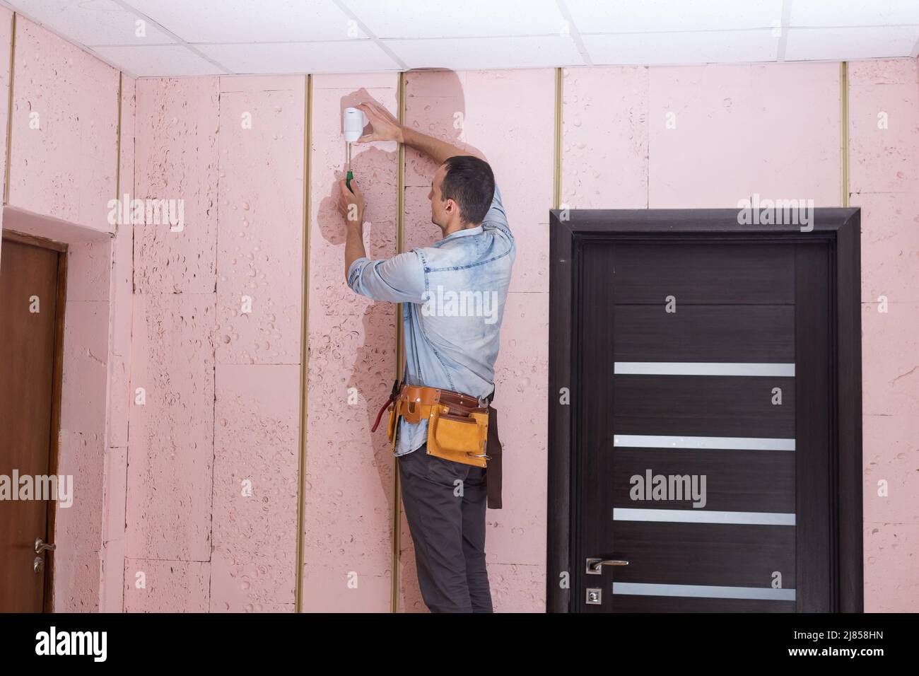 Young electrician installing security alarm on wall. Stock Photo