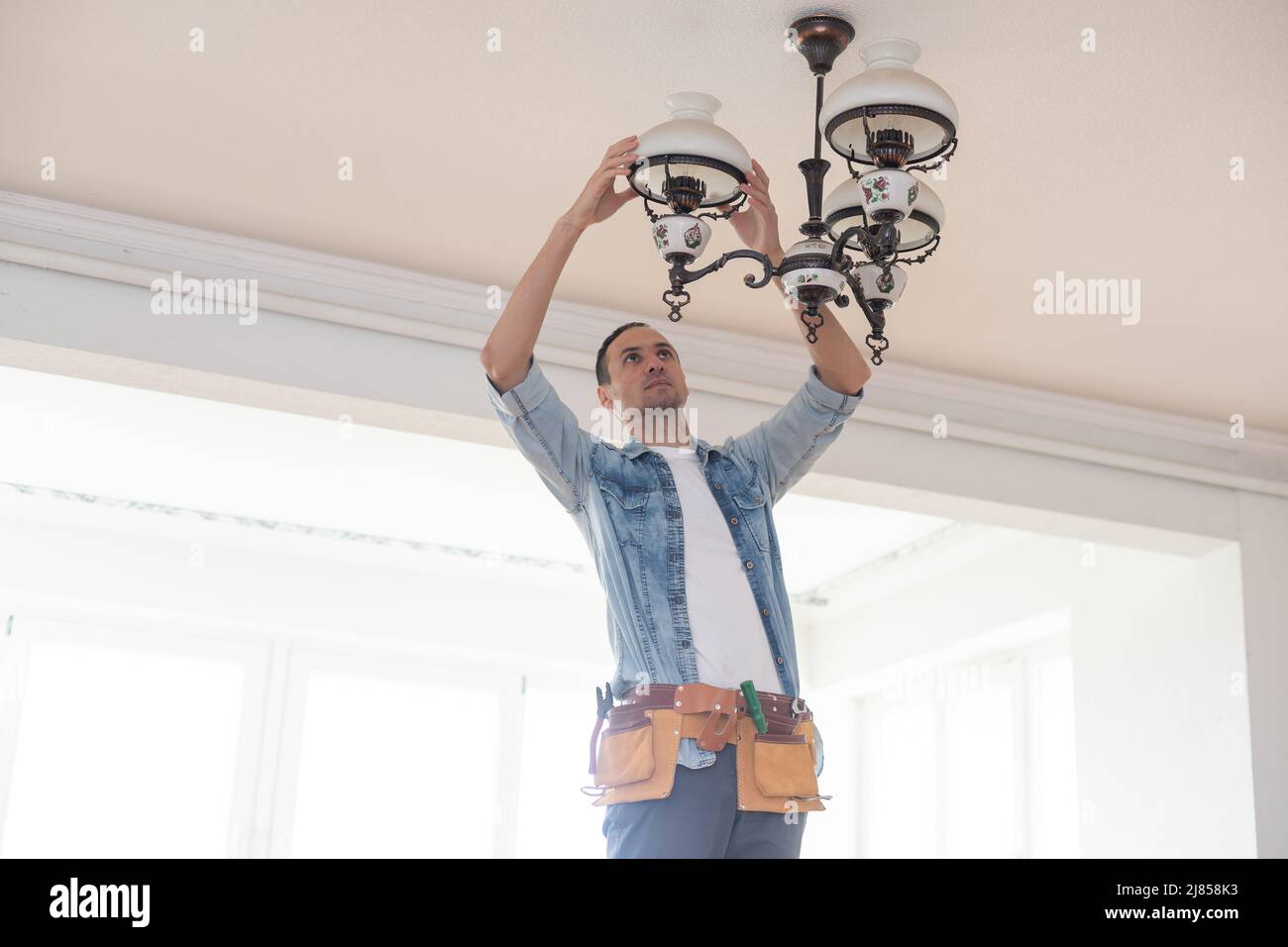 An electrician fixing wires, installing light on the ceiling Stock Photo