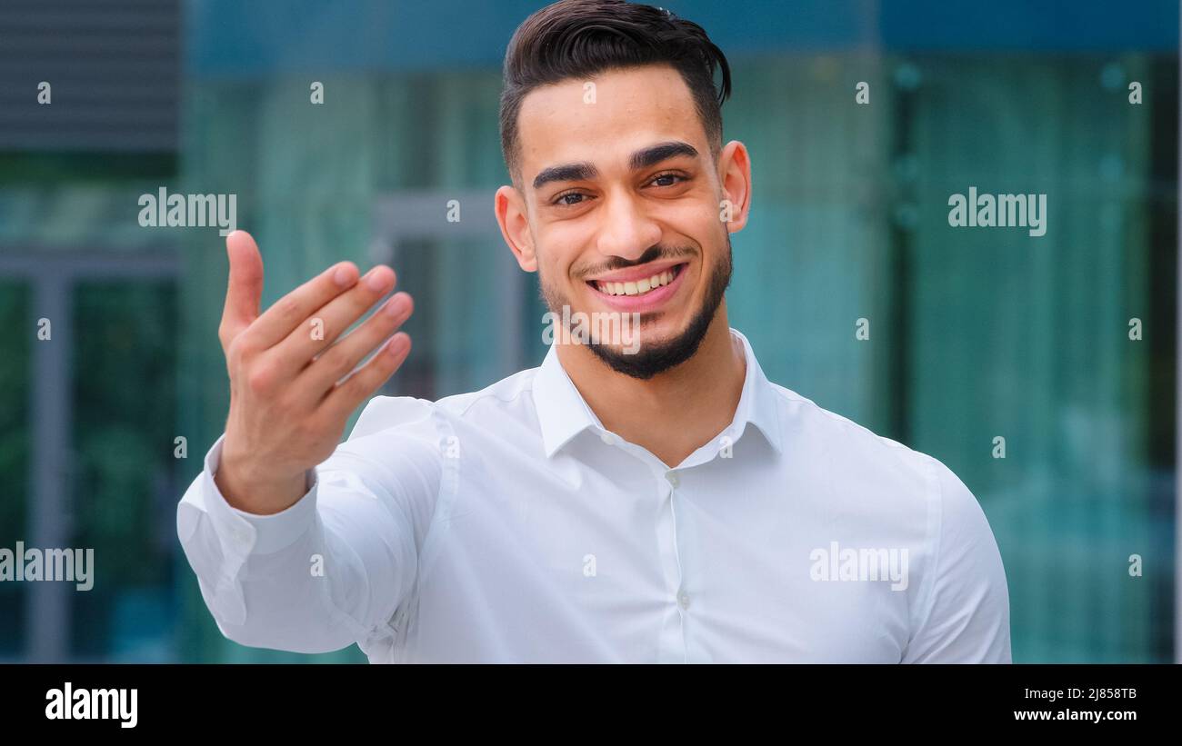 Portrait friendly smiling toothy hispanic arab business man spaniard boss wears white formal shirt showing gesture of invitation advice to approach Stock Photo