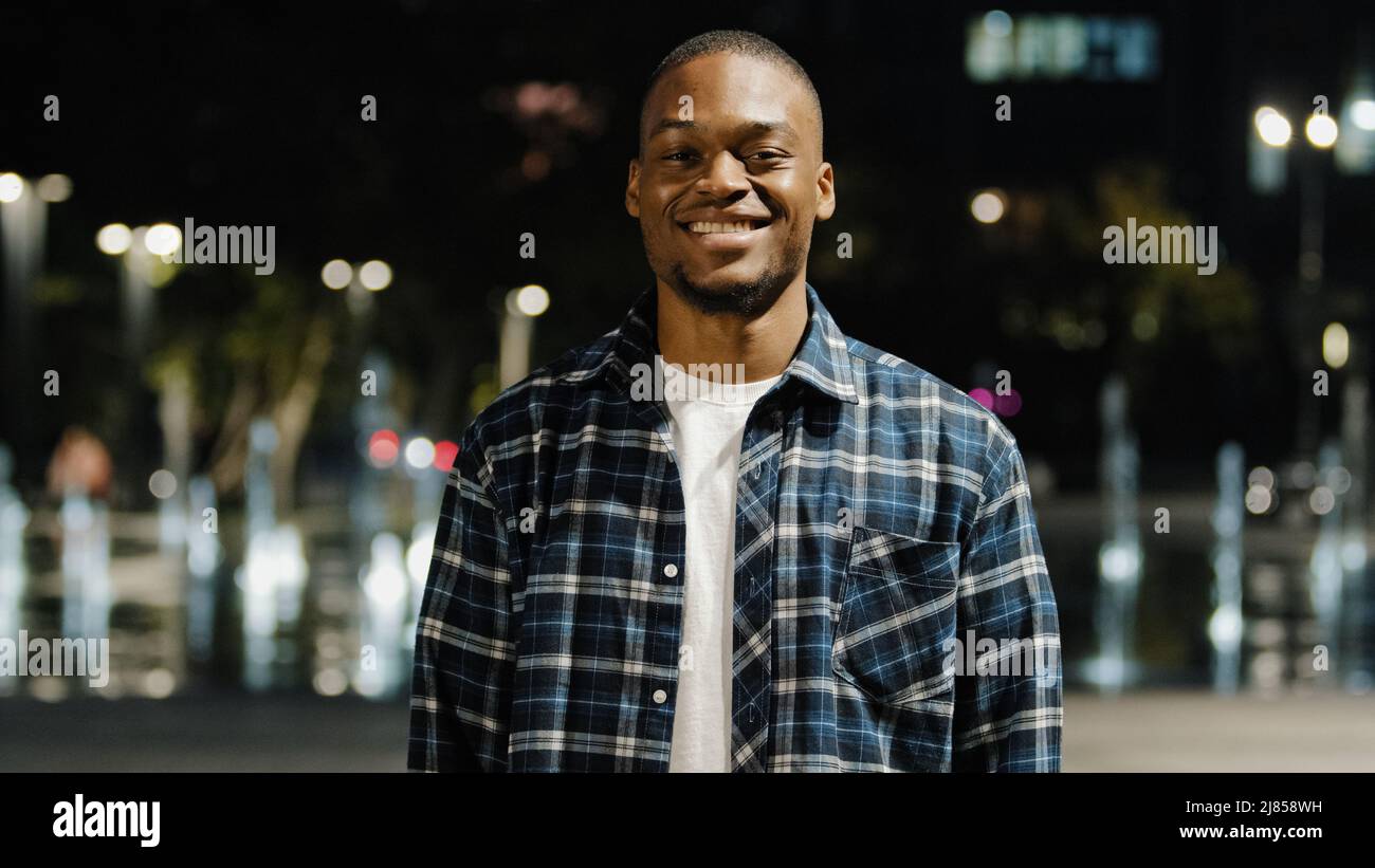 Portrait african american 20s millennial satisfied man handsome guy tourist stands in city in evening background looking at camera smiling toothy Stock Photo