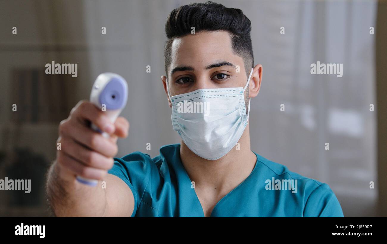 Arabian male medical worker doctor surgeon man in protective mask taking temperature with non-contact infrared digital thermometer during covid-19 Stock Photo
