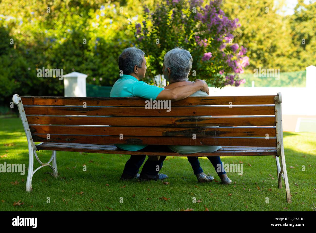 Biracial senior husband with hand on senior wife's shoulder sitting on bench against trees in park Stock Photo