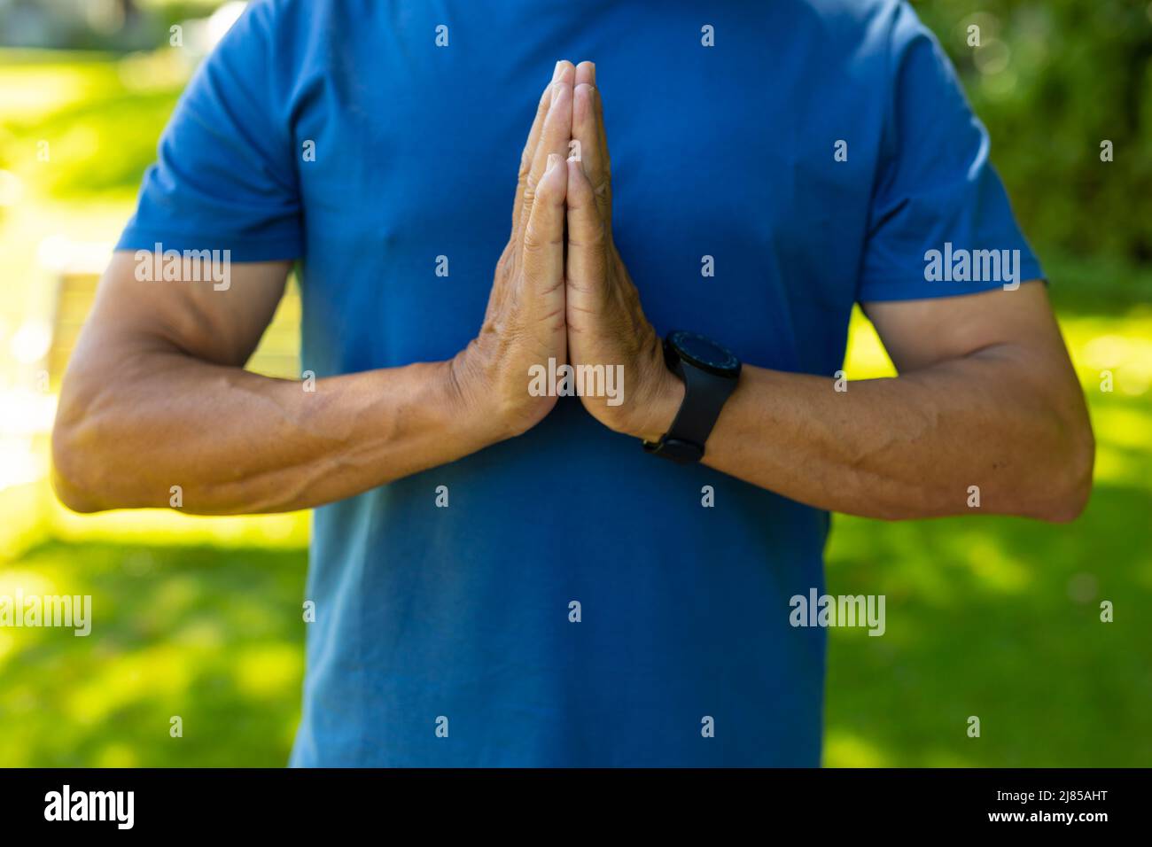 Midsection of biracial senior man wearing blue sports clothing standing in prayer position at yard Stock Photo