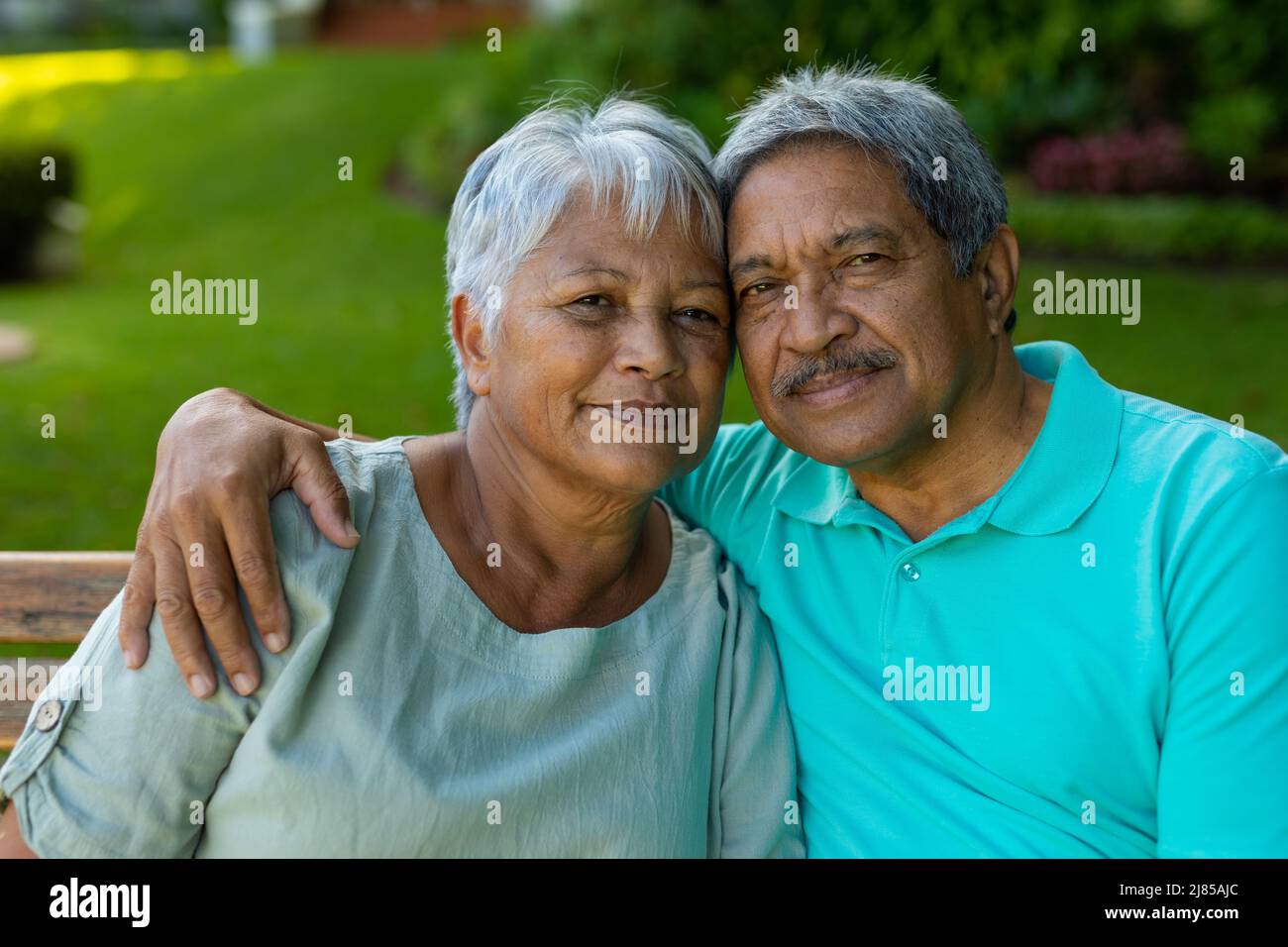 Close-up portrait of loving senior man with hand on wife's shoulder sitting on bench in park Stock Photo