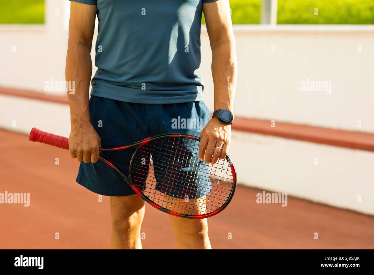 Midsection of biracial senior man wearing sports clothing holding racket while standing in court Stock Photo