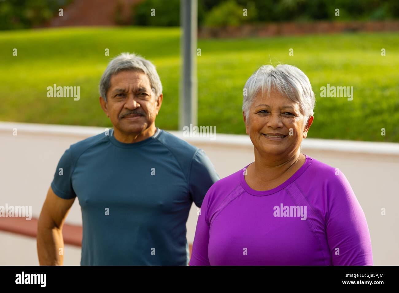 Portrait of biracial senior woman and man wearing sports clothing standing in tennis court Stock Photo