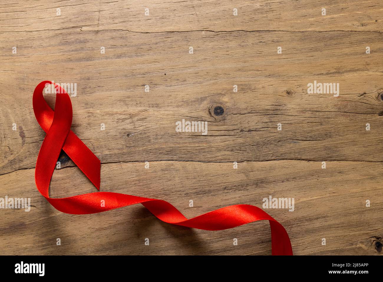 Directly above shot of single red aids awareness ribbon on wooden table, copy space Stock Photo