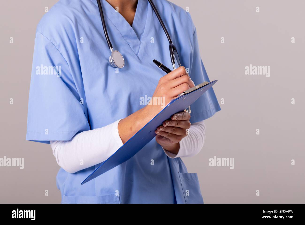 Midsection of african american mid adult female doctor with stethoscope writing on clipboard Stock Photo
