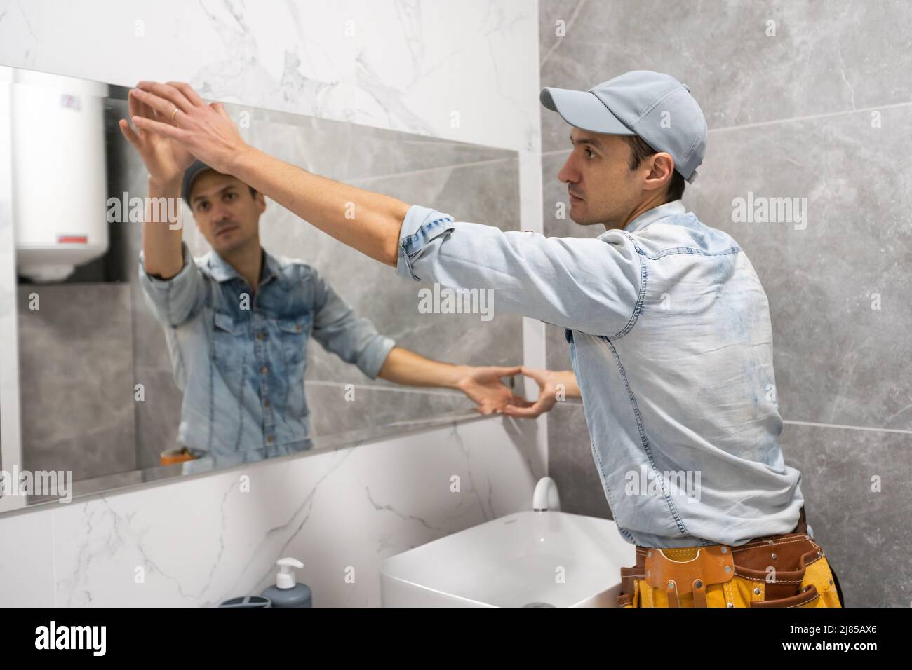 The worker installs the mirror in the bathroom Stock Photo Alamy